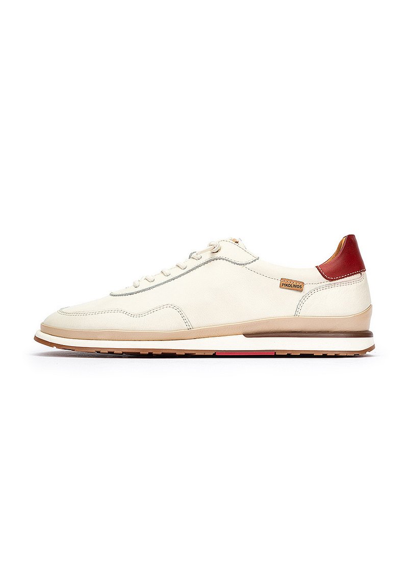 Zapatilla de cuero blanca con suela marrón claro, acento en el talón rojo y costura gris; presenta cordones planos y un diseño de punta redondeada.
