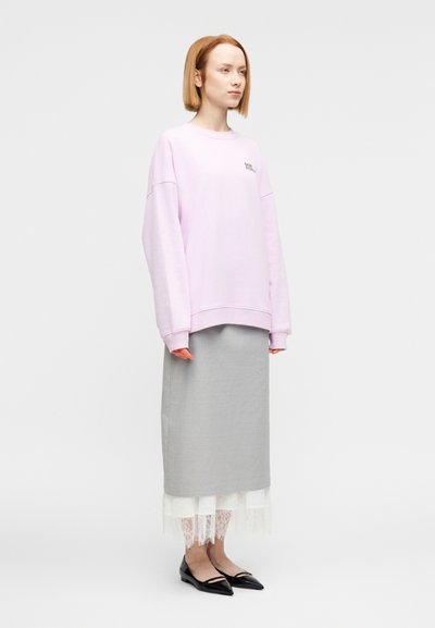 Ροζ ανοιχτόχρωμο φαρδύ φούτερ με φαρδιές ραφές στους ώμους, συνδυασμένο με γκρι μίντι φούστα που έχει λευκή δαντέλα και μαύρα μυτερά παπούτσια μπαλάκια.