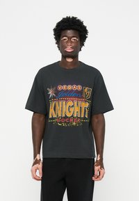 Black cotton t-shirt featuring bold multicolored print with "VEGAS GOLDEN KNIGHTS HOCKEY" text, short sleeves, loose fit. Casual style.