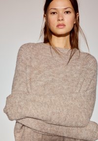 Svetlo béžový nadmerný pletený sveter s rebrovanou textúrou a širokými rukávmi, s jednoduchým okrúhlym výstrihom a mäkkou tkaninou.