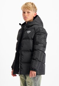 Zwarte pufferjack met een capuchon, voorzien van een ritsluiting, elastische manchetten en een logo op de borst. Het materiaal is glanzend en gewatteerd.