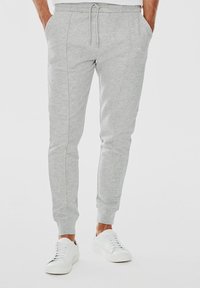 Jasnoszare dresy wykonane z miękkiego materiału, dopasowany krój z kieszeniami bocznymi, elastyczny pas ze sznurkiem oraz ściągacze przy nogawkach.