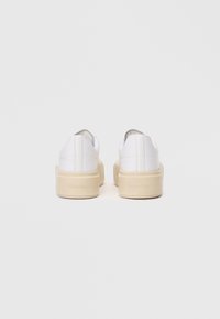 Λευκά slip-on παπούτσια με λεία δερμάτινη επιφάνεια, με χοντρή κρέμ πλατφόρμα και διακριτές ραφές.