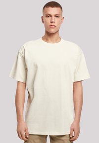 Beige übergroßes Baumwoll-T-Shirt mit kurzen Ärmeln, rundem Ausschnitt und glatter Textur. Keine sichtbaren Logos oder Muster. Einfaches Design.