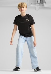 Černé bavlněné tričko s logem "PUMA", světle modré džíny a černé tenisky. Celkový outfit má neformální, uvolněný střih.