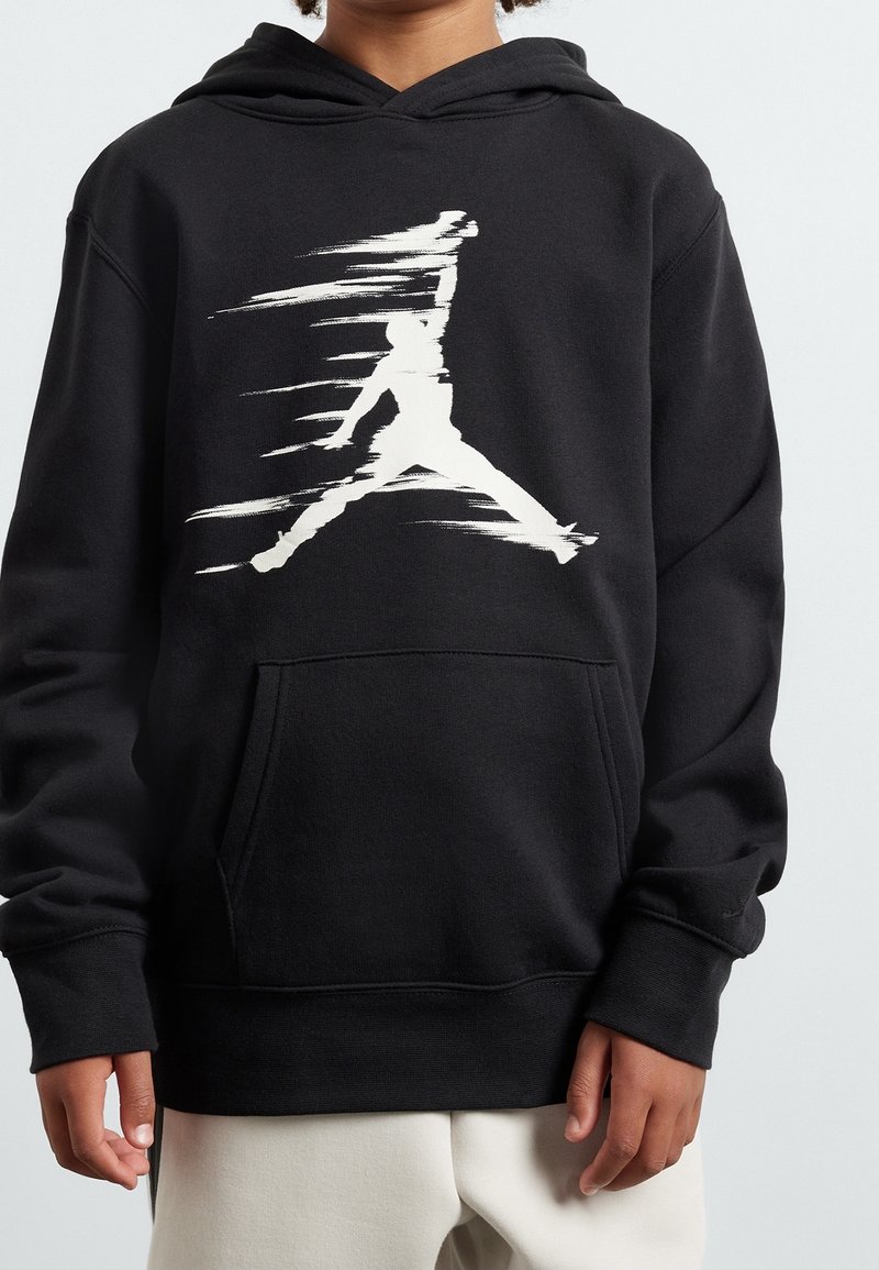 Sweat à capuche noir porté par un enfant avec une silhouette blanche floue d'une figure sautante sur la poitrine et la poche kangourou avant.