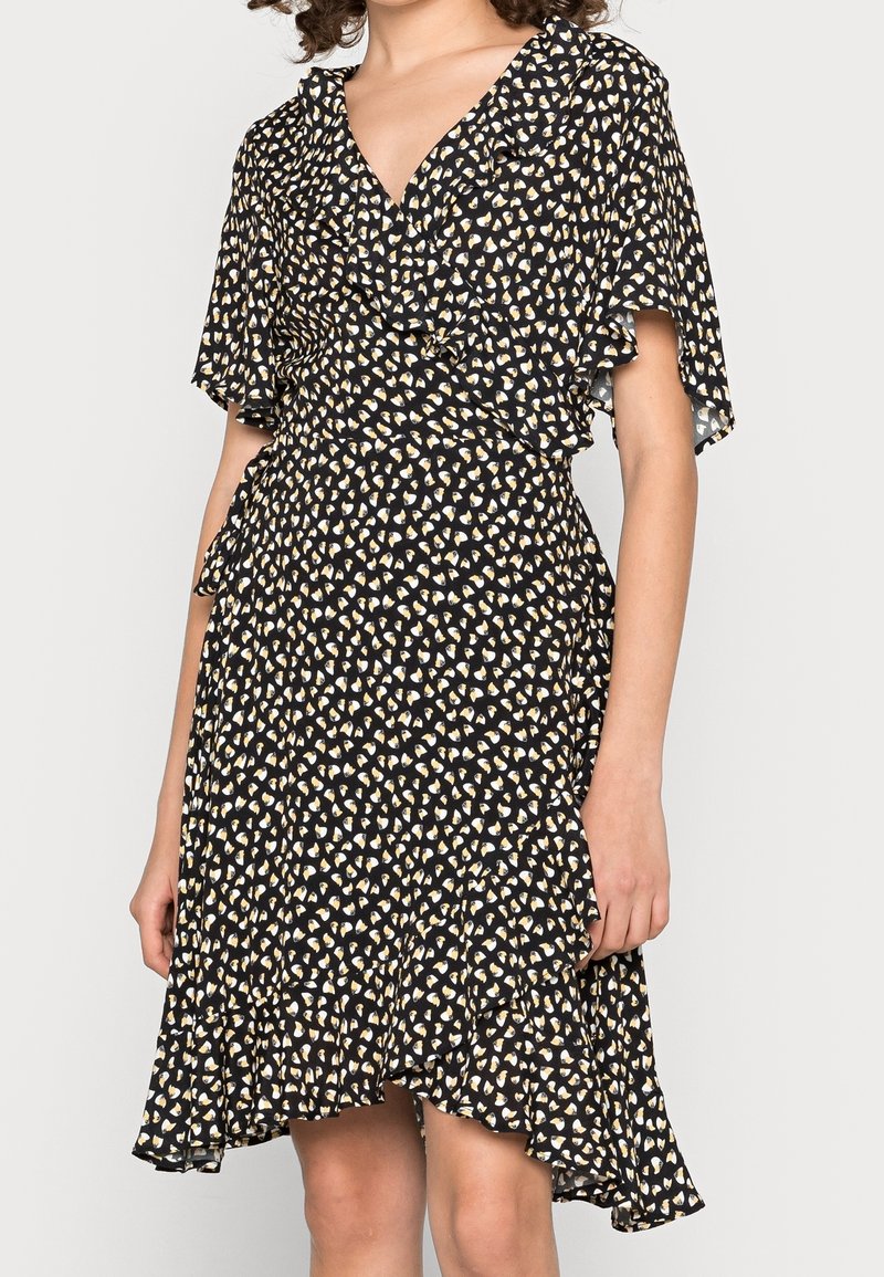 Robe noire avec un décolleté en V et des manches volantées, ornée d'un motif en cœur doré et blanc sur un tissu léger. Ourlet évasé.