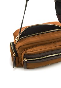 Borsa in nylon marrone con più scomparti, zip dorate, accentuazioni testurizzate e una tracolla removibile, posizionata su uno sfondo bianco.