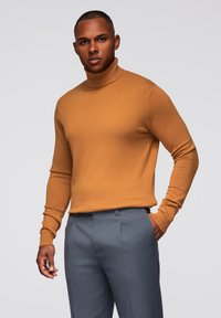 Rollkragenpullover in Senfgelb, aus weichem Material, kombiniert mit maßgeschneiderten grauen Hosen, die ein figurbetontes, glattes Design aufweisen.