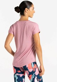 Camiseta atlética de manga corta en rosa claro con un corte relajado, combinada con leggings de patrones multicolores que presentan diseños florales sobre un fondo oscuro.