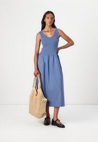 Sleeveless blue cotton dress with a gathered waist, paired with a woven beige tote bag and black shoes. Simple, clean design.