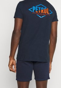Mörkblå bomullströja med en stor, flerfärgad "PETROL" grafisk design och text på baksidan, i kombination med matchande mörkblå shorts.