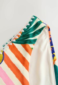 Színes bikini alsó trópusi mintával, zöld levelekkel és élénk csíkokkal. Texturált varrás a derékszegély mentén.