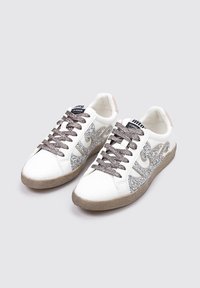 Baskets blanches avec des accents en paillettes argentées et un design ondulé. La chaussure est dotée d'une semelle beige texturée et de lacets gris.