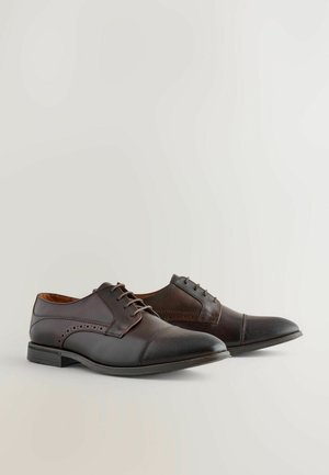 Zapatos de cuero marrón oscuro con un acabado suave, presentan una punta afilada, una puntera texturizada y perforaciones decorativas en el lateral.