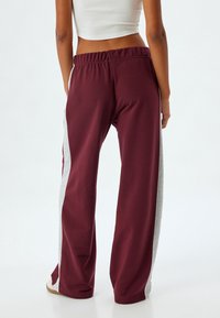 Bordeaux sweatpants met een relaxte pasvorm, voorzien van grijze zijstrepen en een elastische tailleband. De stof lijkt zacht en ademend te zijn.