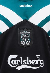 Roheline ja must Liverpool FC jalgpallimärk Adidas logo, klubi vapp ja Carlsbergi sponsori tekstiga ees.