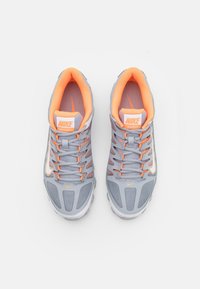 Par de zapatillas de entrenamiento Nike en gris y naranja vistas desde arriba sobre un fondo blanco, mostrando los detalles de los cordones y el logo.