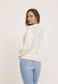 Pull en tricot blanc avec un design en mailles ouvertes, col et ourlet côtelés, accentué d'une bande orange. Associé à un jean ajusté bleu clair.