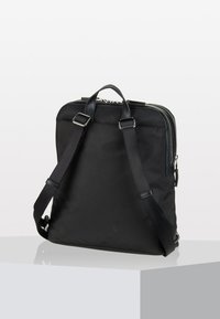 Zaino nero con spallacci regolabili, manico superiore e chiusura con zip. Materiale in tessuto liscio con un design minimalista. Silhouette semplice.
