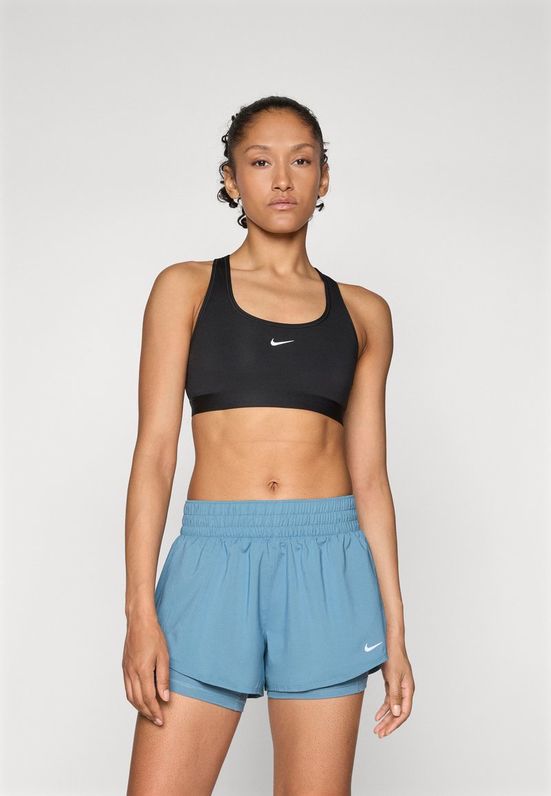 Crni sportski grudnjak s Nike logotipom i svijetloplave atletske kratke hlače s elastičnom trakom u struku i Nike logotipom. Glatki materijal, pripijeni kroj.