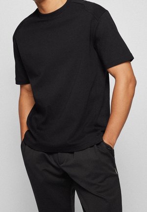 T-shirt noir à manches courtes en coton doux, avec un col rond et des détails de couture subtils, associé à un pantalon sombre.