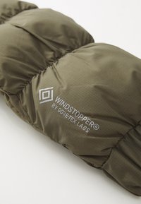 Olivově zelená pufrovací látka s jemným leskem, šité sekce, obsahuje logo "WINDSTOPPER® by GORE-TEX LABS" v stříbrné barvě. Měkká textura.