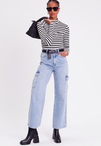 Langsleeve, zwart-wit gestreept shirt, high-waisted lichtblauwe cargobroek, zwarte riem, zwarte haklaarzen en een kleine zwarte tas.