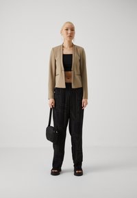 Beige cropped blazer with a tailored fit, black crop top, black pants featuring a graphic print, and a small black crossbody bag.
