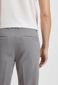 Gray trousers with a smooth texture, featuring two back pockets and a subtle brand tag. The waistband has belt loops.