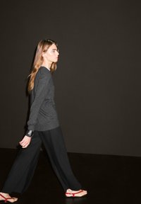 Maglietta grigia a maniche lunghe abbinata a pantaloni neri larghi e sandali rossi. L'insieme presenta una vestibilità rilassata e un design minimalista.