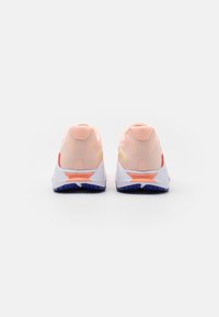 Un paio di scarpe da ginnastica rosa e bianche viste da dietro, con suole spesse caratterizzate da battistrada blu e dettagli arancioni.