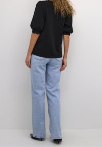 Svart topp med puffärmar i kombination med ljusblå vida jeans. Toppen är i mjukt tyg med en avslappnad passform, och jeansen har synliga sömmar.