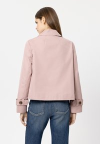 Light pink cropped jacket with a notched collar and buttoned cuffs, featuring a smooth texture and a sleek design. Paired with blue jeans.