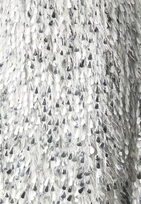 Tissu en sequins argentés avec une surface texturée. Présente des sequins réfléchissants en forme de goutte et des accents en fils fins et minces.