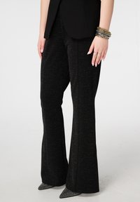 Zwarte uitlopende broek met een gestructureerde stof met metallic spikkels. Gecombineerd met een zwarte blazer en puntige schoenen.