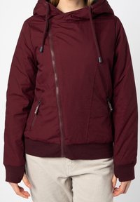 Maroon huva jacka med frontblixtlås, två fickor med blixtlås på sidorna, ribbad ärm- och nederkant, tillverkad av ett lätt, texturerat tyg.