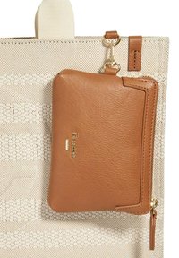 Portefeuille en cuir brun avec une fermeture éclair, présentant un logo doré, attaché à un sac fourre-tout beige texturé avec un motif design.