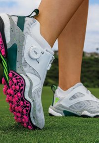 Golfskor med övre del i vit mesh, gröna accenter och rosa spikar. Utrustad med BOA-snörsystem och strukturerad sula för grepp.