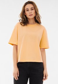 Korte mouwen, boxy t-shirt van lichtgele katoen met een ronde halslijn en een rechte zoom, gecombineerd met zwarte spijkerbroeken.