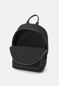Zaino in tessuto nero con forma arrotondata, chiusura con zip e tasca frontale piatta. Dotato di manico superiore e rivestimento interno liscio.