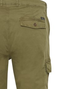 Pantalones cargo verde oliva hechos de una mezcla de algodón, que cuentan con un bolsillo trasero con solapa y cierre de botón, y un bolsillo cargo lateral.