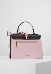 Różowa usztywniana torebka z czarną górą, złotymi elementami, przednią kieszenią na zamek i wzorzystym szalikiem przy uchwycie.