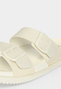 Sandale slide blanc cassé avec deux larges brides comportant de grandes boucles ajustables et une semelle texturée pour une bonne adhérence.