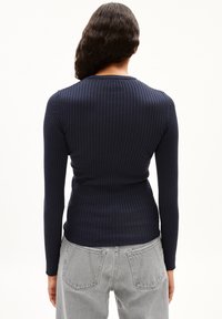 Personne vue de dos portant un haut à manches longues côtelé bleu marine et un jean en denim gris clair avec des poches arrière.