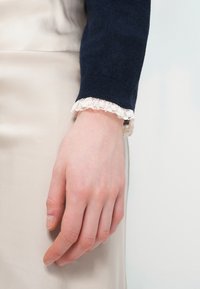 Πουλόβερ σε ναυτικό μπλε με δαντελένιο τελείωμα στο μανίκι, σε αντίθεση με απαλό μπεζ σατέν ύφασμα. Λείο υφή, εφαρμοστό σχέδιο.