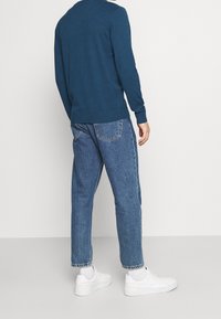 Maglione blu a maniche lunghe con scollatura rotonda, abbinato a jeans in denim azzurro e sneakers bianche, visto da dietro.