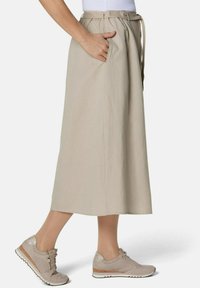 Beige, knielanger Rock aus leichtem Stoff mit Seitentaschen und einem Gürtel in der Taille. Kombiniert mit hellbeigen Sneakers.