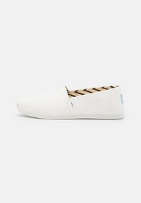 Hvite lær slip-on sko med avrundet tå, med skrå syddetaljer og et teksturert brunt og svart stripet interiør.