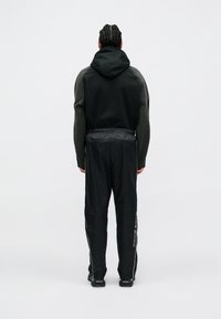 Mustmust musta kapuuts, millel on tekstuuriga hallid varrukad, koos mustade läikivate treeningpükstega, millel on külgsiribad. Tagantvaates on rõhutatud üldine sobivus.